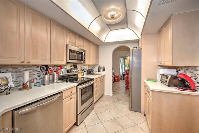 kitchen featuring arched walkways, stainless steel appliances, light brown cabinetry, and light tile patterned flooring