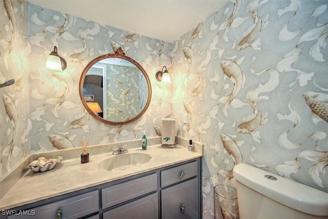 bathroom with vanity, toilet, and wallpapered walls