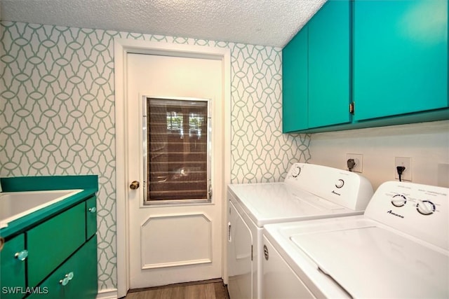 washroom featuring a textured ceiling, washing machine and dryer, cabinet space, and wallpapered walls