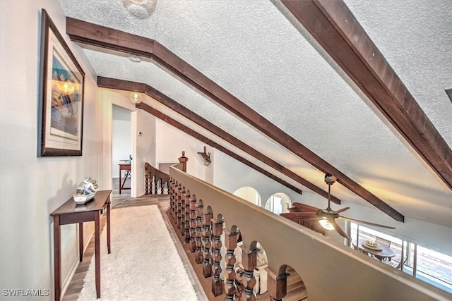 interior space with light wood-style floors, lofted ceiling with beams, an upstairs landing, and a textured ceiling