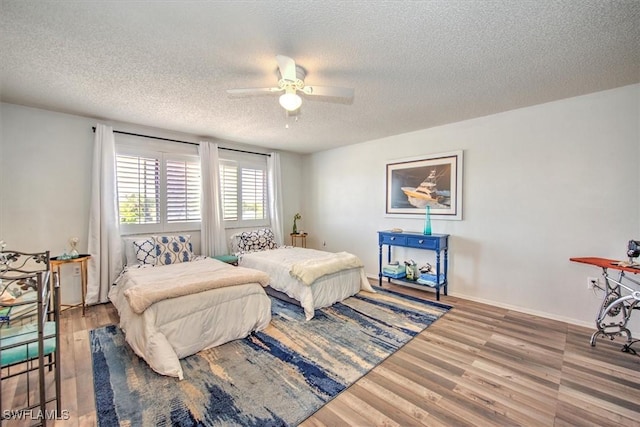 bedroom featuring ceiling fan, a textured ceiling, baseboards, and wood finished floors