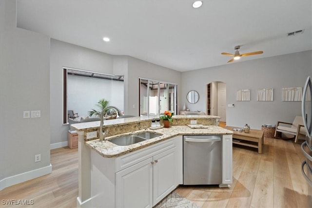 kitchen featuring arched walkways, light wood finished floors, stainless steel dishwasher, white cabinets, and a sink