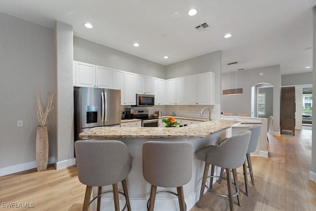 kitchen with a breakfast bar, visible vents, light wood-style flooring, backsplash, and appliances with stainless steel finishes