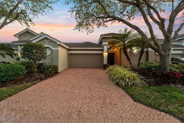 view of front of house featuring decorative driveway, an attached garage, and stucco siding