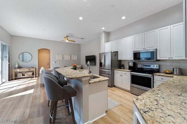 kitchen with arched walkways, appliances with stainless steel finishes, light wood-type flooring, and a sink