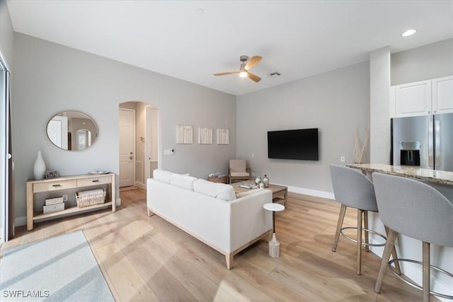 living room featuring arched walkways, recessed lighting, a ceiling fan, light wood-type flooring, and baseboards