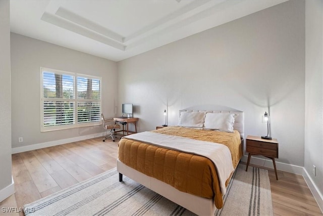 bedroom featuring light wood finished floors, baseboards, and a tray ceiling