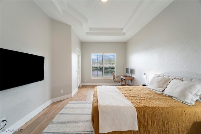 bedroom featuring light wood-style floors, baseboards, and a tray ceiling