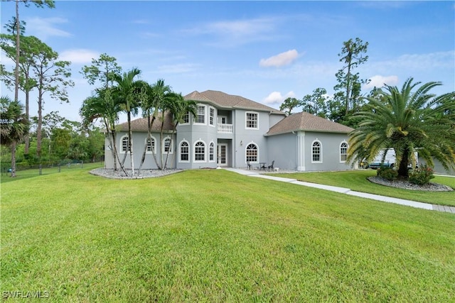 rear view of property with a balcony, stucco siding, and a yard