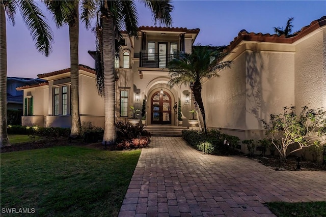 view of front of house with french doors, a lawn, a balcony, and stucco siding