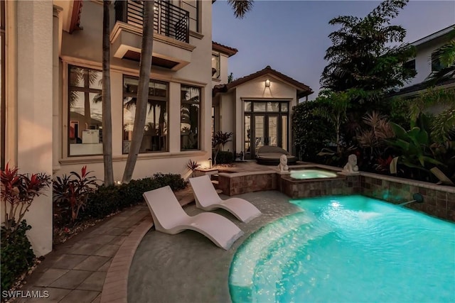 pool at dusk with a pool with connected hot tub