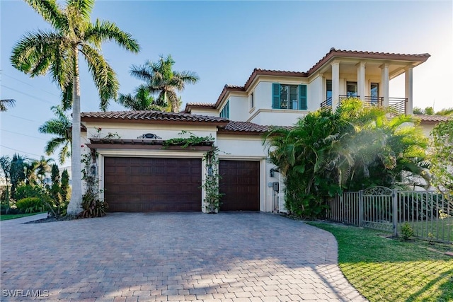 mediterranean / spanish house featuring decorative driveway, a tile roof, fence, and stucco siding