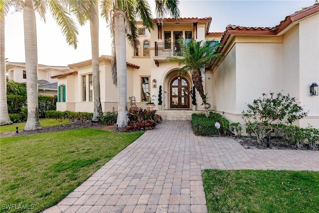 view of exterior entry with a yard, a balcony, and stucco siding