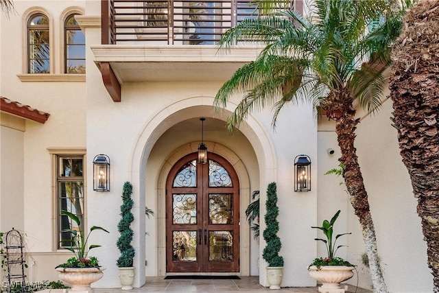 view of exterior entry with french doors, a balcony, and stucco siding