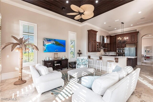 living area featuring arched walkways, crown molding, visible vents, baseboards, and ceiling fan with notable chandelier