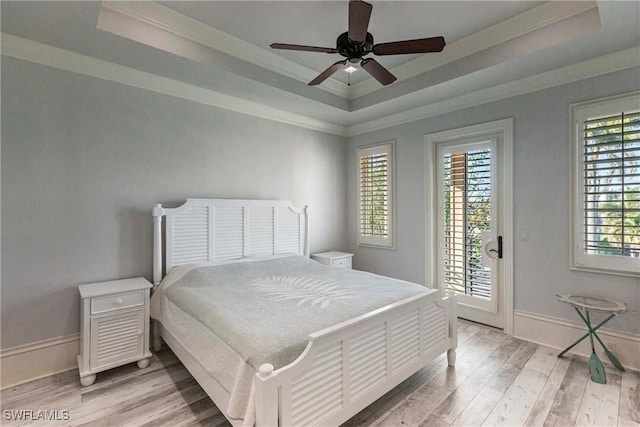 bedroom featuring access to exterior, light wood-style flooring, a tray ceiling, and ornamental molding