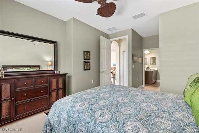 bedroom featuring arched walkways, light colored carpet, visible vents, a ceiling fan, and ensuite bath