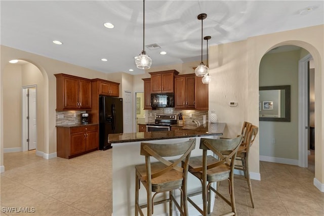 kitchen with arched walkways, black appliances, dark stone countertops, a peninsula, and a kitchen breakfast bar