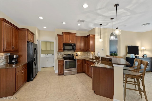 kitchen featuring washer and clothes dryer, a breakfast bar area, visible vents, a peninsula, and black appliances