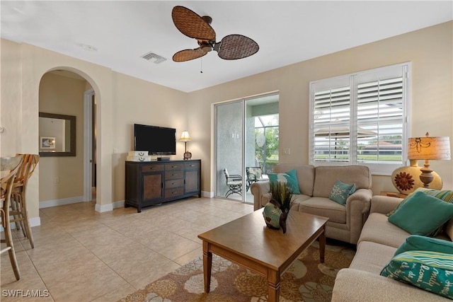 living area with arched walkways, light tile patterned flooring, visible vents, and baseboards