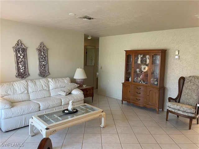 living area featuring visible vents, a textured wall, and light tile patterned floors