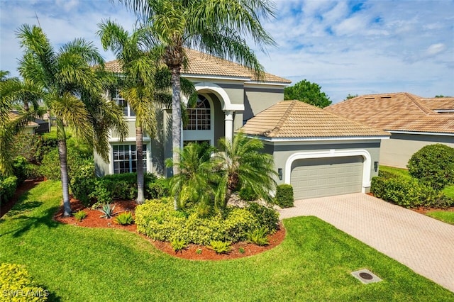 mediterranean / spanish house with a garage, decorative driveway, a front lawn, and stucco siding