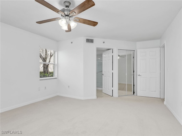 unfurnished bedroom featuring light colored carpet, visible vents, a spacious closet, a ceiling fan, and baseboards