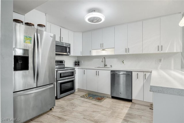 kitchen featuring light countertops, decorative backsplash, appliances with stainless steel finishes, white cabinetry, and a sink