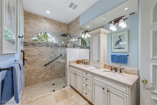 bathroom featuring double vanity, tiled shower, a sink, and visible vents