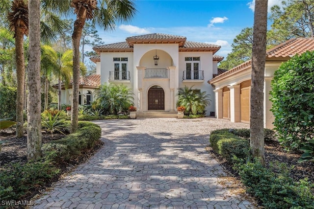 mediterranean / spanish-style home with a balcony, a tiled roof, decorative driveway, and stucco siding