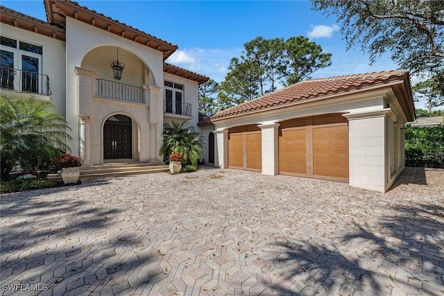 mediterranean / spanish-style house featuring a garage, a balcony, a tiled roof, an outdoor structure, and stucco siding