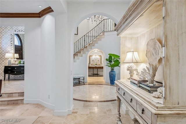 hall featuring baseboards, arched walkways, a towering ceiling, ornamental molding, and stairs