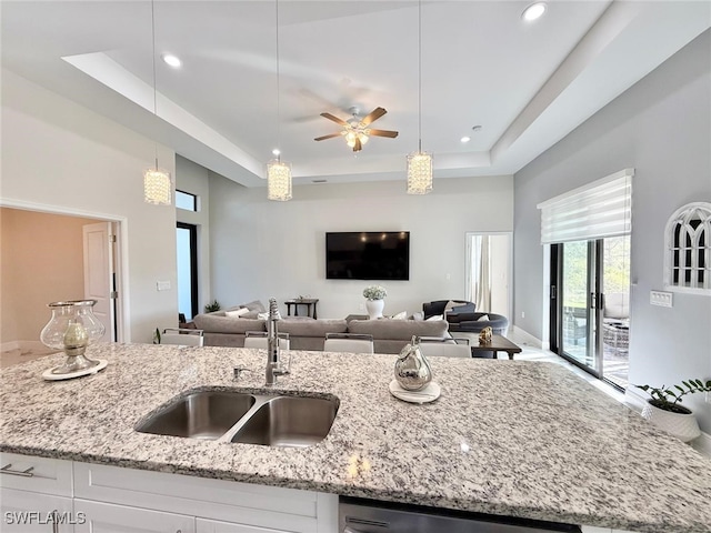 kitchen featuring light stone counters, pendant lighting, a raised ceiling, open floor plan, and a sink