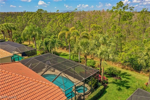 view of pool with a patio area, a lanai, a pool with connected hot tub, and a view of trees