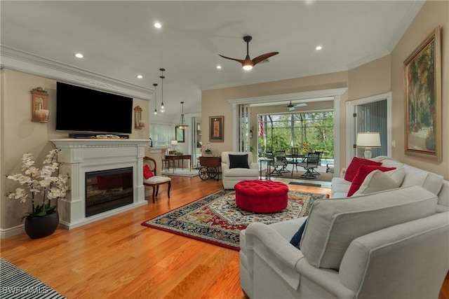 living area with ceiling fan, wood finished floors, a glass covered fireplace, and ornamental molding