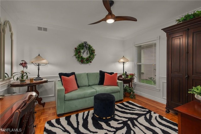 living area with a wainscoted wall, crown molding, visible vents, a decorative wall, and ceiling fan