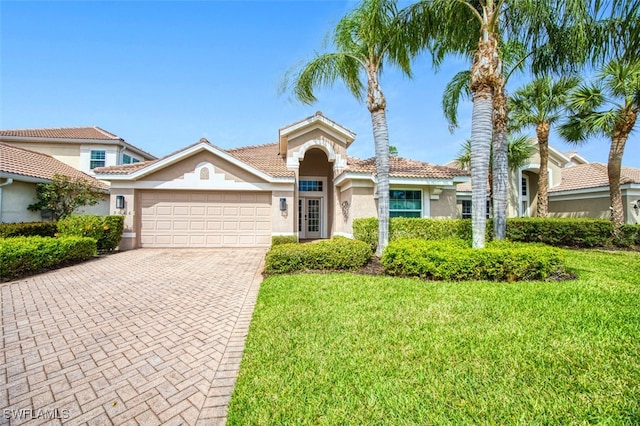 mediterranean / spanish-style house with a front lawn, decorative driveway, an attached garage, and stucco siding