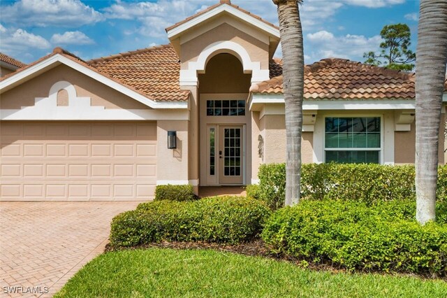 view of exterior entry featuring a garage, decorative driveway, a tiled roof, and stucco siding