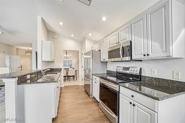 kitchen with vaulted ceiling, stainless steel appliances, light wood-style floors, white cabinetry, and a sink