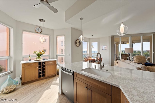 kitchen featuring dishwasher, light wood-style flooring, light stone counters, brown cabinets, and a sink