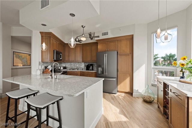 kitchen with light wood finished floors, decorative backsplash, appliances with stainless steel finishes, a sink, and a peninsula