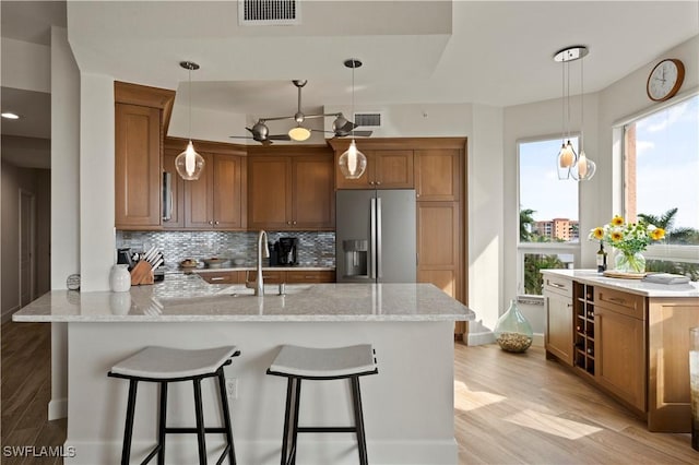 kitchen with a peninsula, a sink, visible vents, stainless steel refrigerator with ice dispenser, and backsplash