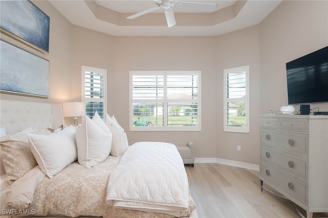 bedroom with light wood finished floors, multiple windows, a raised ceiling, and baseboards