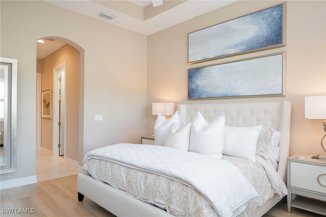 bedroom featuring arched walkways, light wood finished floors, visible vents, and baseboards