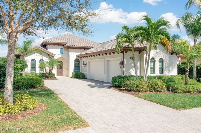 mediterranean / spanish-style house featuring a garage, stucco siding, decorative driveway, and a tiled roof