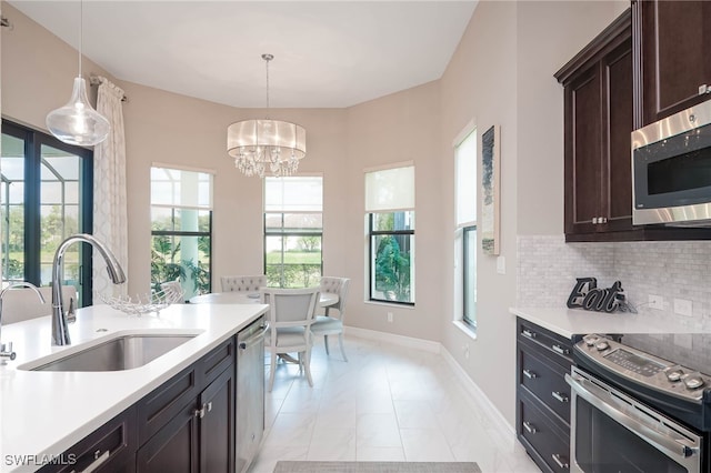 kitchen with a sink, light countertops, appliances with stainless steel finishes, tasteful backsplash, and decorative light fixtures