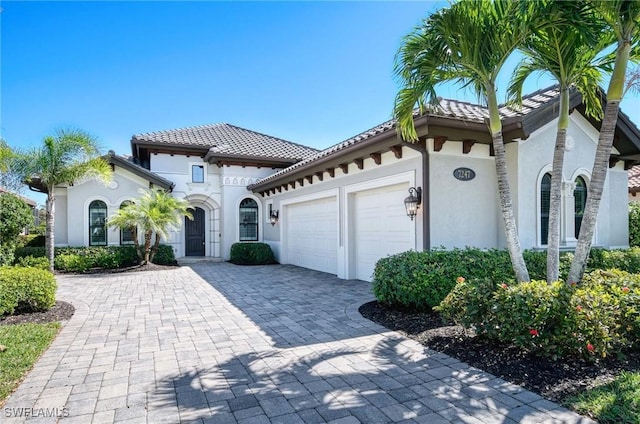 mediterranean / spanish-style house featuring stucco siding, an attached garage, a tile roof, and decorative driveway