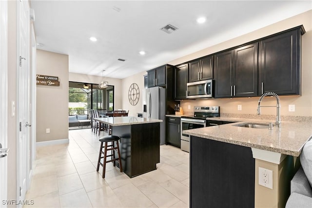 kitchen featuring light stone counters, a breakfast bar area, a sink, visible vents, and appliances with stainless steel finishes