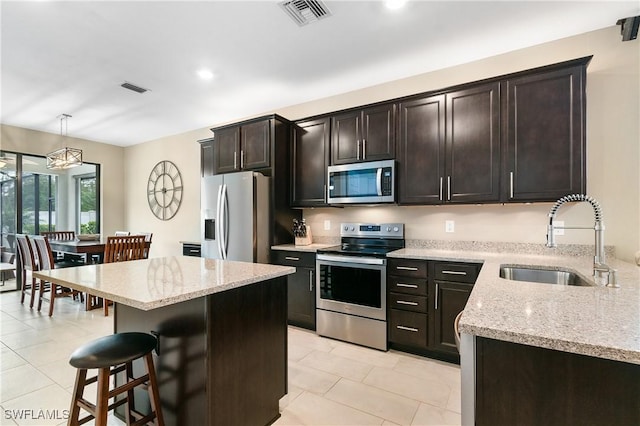 kitchen featuring visible vents, appliances with stainless steel finishes, a sink, light stone countertops, and a kitchen bar