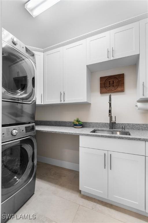 washroom featuring light tile patterned floors, cabinet space, stacked washer / dryer, a sink, and baseboards